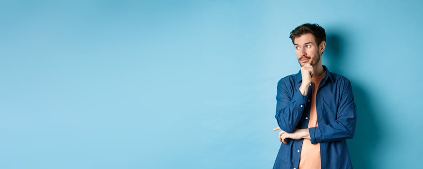 Thoughtful caucasian man looking aside at empty space and thinking, standing pensive on blue background photo