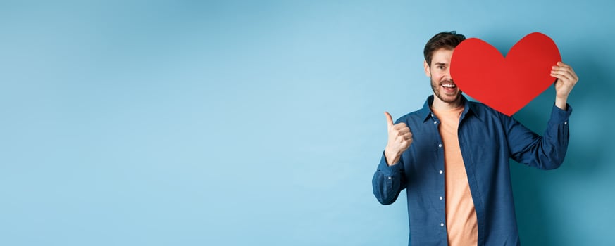 Happy man showing valentines heart and thumbs-up gesture, standing over blue background photo