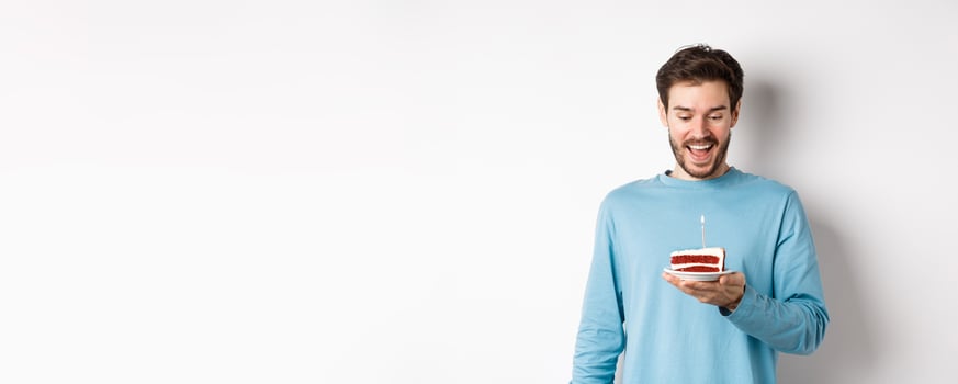 Cheerful man looking happy at birthday cake, celebrating bday, standing over white background photo