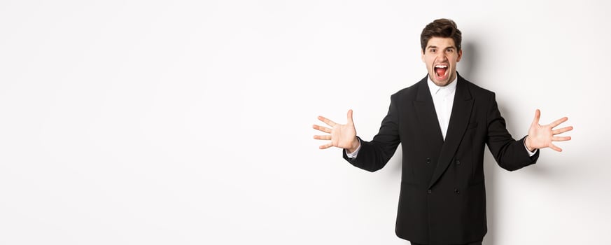 Portrait of pissed-off and frustrated businessman in suit, shouting angry and shaking hands, standing distressed against white background photo