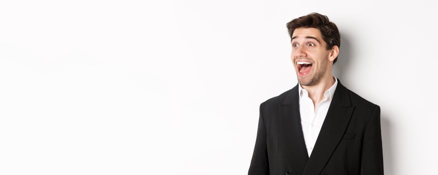 Close-up of handsome male entrepreneur in suit, looking left and smiling amazed, standing against white background photo
