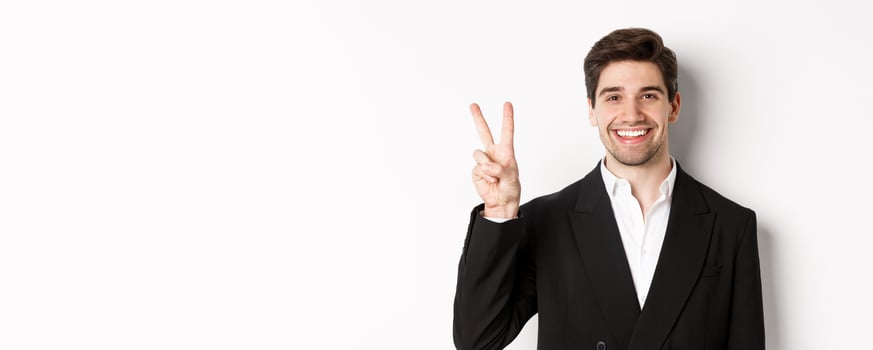Close-up of handsome businessman in black suit, smiling amazed, showing number two, standing over white background photo