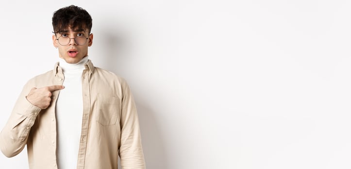 Confused and surprised young man pointing at himself, being chosen or accused, standing on white background photo