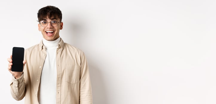 Technology and online shopping concept. Cheerful handsome guy in glasses showing empty smartphone screen and smiling, showing application, standing on white background photo