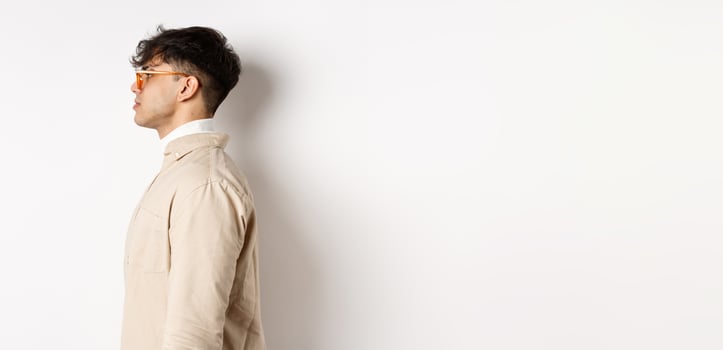 Profile of handsome caucasian man in eyewear, looking at empty space left with serious face, standing on white background photo