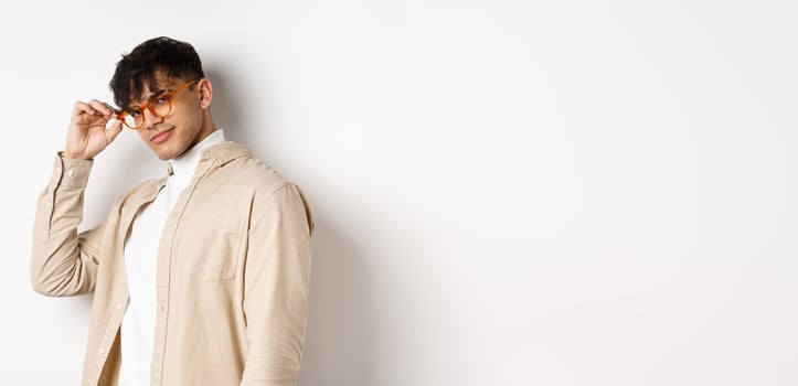 Handsome stylish guy saluting you, touching eyewear and smiling sassy, standing on white background photo
