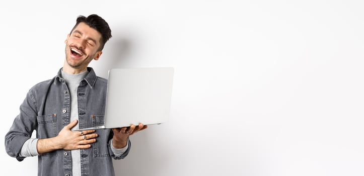 Image of happy guy laughing at funny on laptop, touching belly and smiling satisfied wth good laugh, standing against white background photo