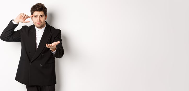 Portrait of confused handsome businessman scolding employee, pointing at head and camera, standing disappointed over white background photo