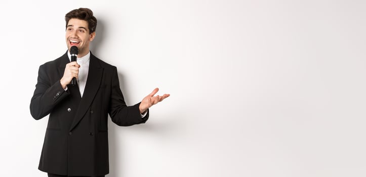 Portrait of handsome man in black suit singing a song, holding microphone and giving speech, standing against white background photo