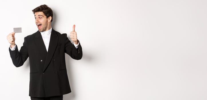 Image of excited handsome businessman, showing credit card and thumb-up, standing against white background photo