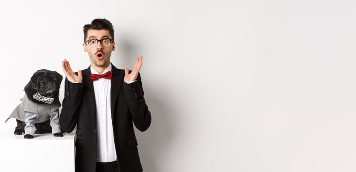 Animals, party and celebration concept. Image of dog owner and cute pug in costumes suits staring surprised at camera, reacting on promo offer, white background photo