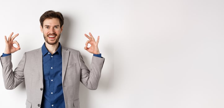 Good choice. Smiling businessman in suit showing okay signs and look happy, recommending good deal, like and approve your choice, standing satisfied on white background photo