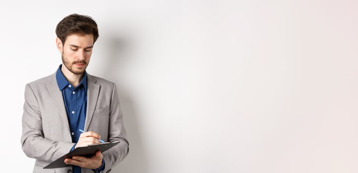 Office worker in suit writing on clipboard, taking notes on meeting, standing on white background photo