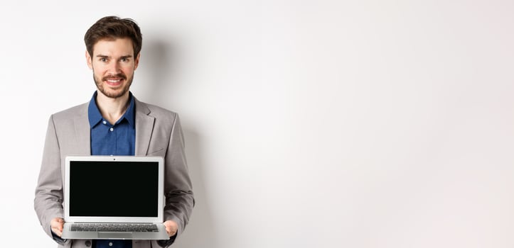 Handsome caucasian businessman in suit showing empty laptop screen, demonstrate promo, standing on white background photo