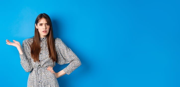 Confused and annoyed girl arguing, raising hand up and frowning, cant understand what big deal, standing on blue background photo