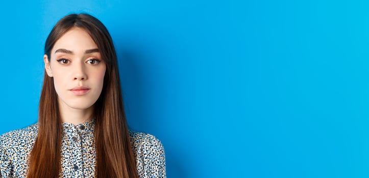 Close-up of candid beautiful woman with long natural hair and makeup, looking at camera, standing on blue background photo