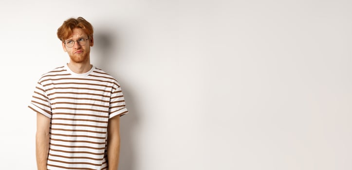 Sad and gloomy redhead man looking upper left corner, sulking and feeling like loser, standing over white background photo