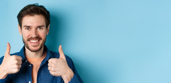 Close-up of smiling good-looking man showing thumbs up, praising good job, recommending company, standing on blue background photo