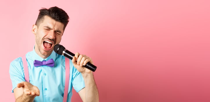 Party and festive events concept. Passionate singer holding microphone and pointing hand at you, singing about love, standing on pink background photo
