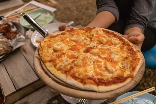 Seafood pizza is served by the staff on a wooden tray that looks appetizing and is a pizza baked in an old-fashioned wood fired oven, giving it the aroma of pizza dough and delicious taste. photo