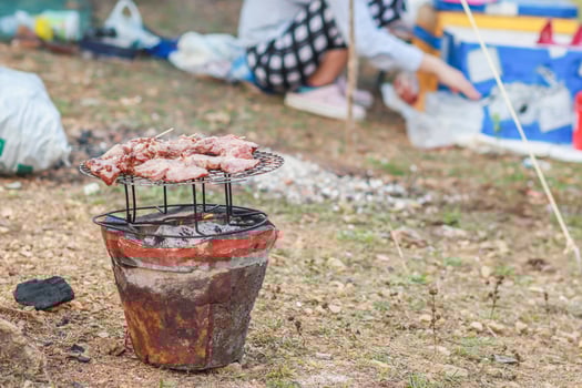 young woman Barbecuing BBQ meat on charcoal grill alone is her responsibility after camping by reservoir. Barbecuing BBQ is popular dish during celebrations and camping. photo