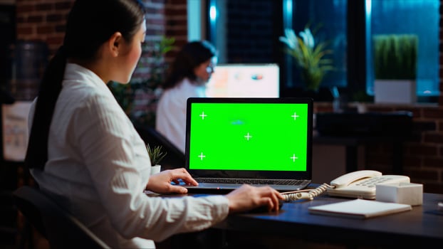 Worker looking over green screen laptop display, researching key data for company project. Businesswoman analyzing figures and charts on chroma key electronic device in office at night photo