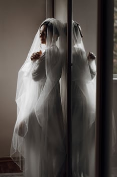 A woman in a white dress is standing in front of a mirror. She is wearing a veil and she is getting ready for a wedding photo