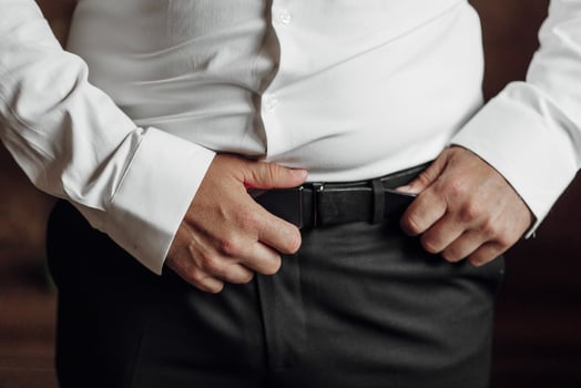 A man in a white shirt and black pants is wearing a belt. He is standing with his hands in his pockets photo