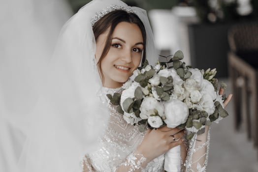 A bride is holding a bouquet of white flowers. She is smiling and looking at the camera photo