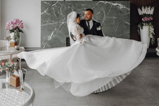 A bride and groom are dancing together in a room with a green wall. The bride is holding her husband's hand and is wearing a white dress photo