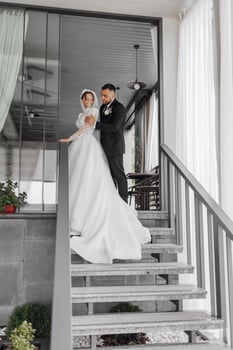 A bride and groom are standing on a set of stairs, with the bride wearing a white dress and the groom wearing a black suit photo