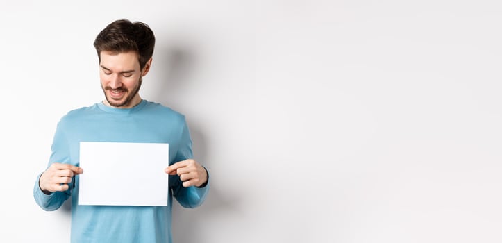 Young caucasian man looking at empty paper, reading logo, standing on white background photo