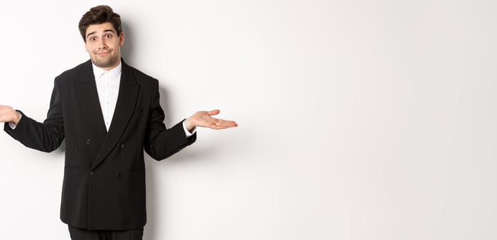 Image of handsome confused man in black suit, shrugging and looking clueless, dont know anything, standing over white background photo