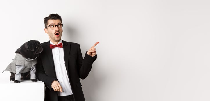 Animals, party and celebration concept. Amazed young man and black dog in costumes staring right at copy space, standing against white background photo