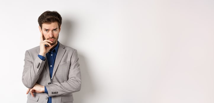 Troubled frowning business man in suit looking at camera pensive, thinking or making decision, standing on white background photo