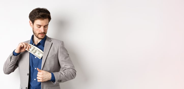 Successful businessman put dollars inside suit pocket, hiding money, standing on white background photo