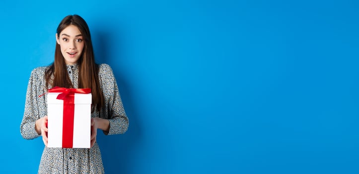 Valentines day concept. Surprised happy girl receiving romantic gift and looking thankful at camera, standing on blue background photo