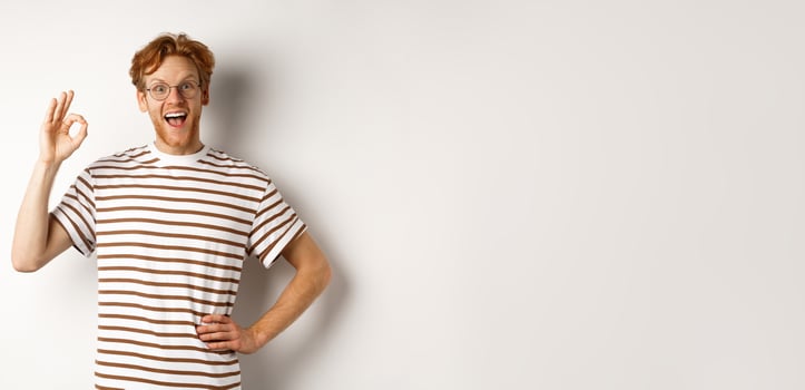 Excellent job. Happy redhead man praising you, showing OK sign and smiling amazed, approve and like something good, standing over white background photo