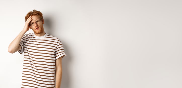 Tired young man student touching head, looking complex and tired, standing over white background photo
