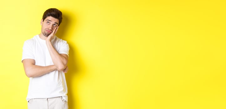 Bored and gloomy guy looking up, imaging things, standing over yellow background photo