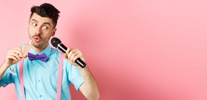 Party and festive events concept. Funny guy singing karaoke, performing song with microphone and drinking champagne from glass, standing on pink background photo