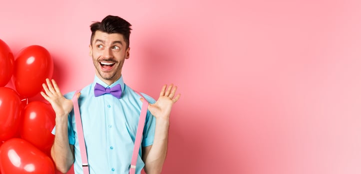 Love and romance concept. Happy man screaming from fantastic news, shouting wow and smiling amused, checking out special offer on Valentines, standing near red hearts balloons photo