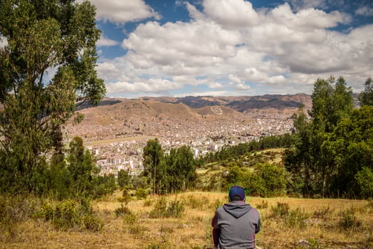 landscape with nearby forest, person sitting and city in the background with mountains, cloudy sky in the background in cusco, peru photo