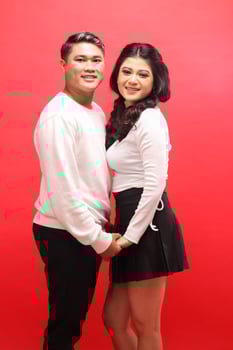 smiling young indonesia couple wearing white sweaters standing facing each other holding hands. for romance, wedding, advertising, promotional content photo