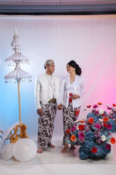 full length of a pair of indonesia men and women smiling at each other wearing modern Javanese traditional clothing, white velvet bridal kebaya, prewedding concept with a white studio background photo