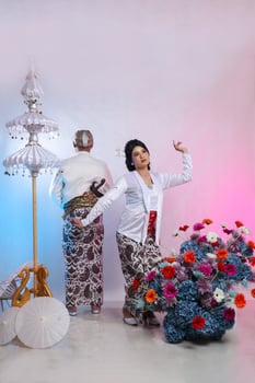 A pair of Asian husband and wife lovers dancing candidly behind a man wearing modern Javanese traditional clothing, white velvet bridal kebaya on a white studio background. for advertising content photo