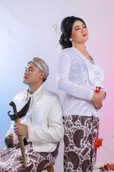 a pair of young Asian man and girl lovers close their eyes candidly wearing modern Javanese traditional clothing, bridal white velvet kebaya on a white studio background. for romance, beauty, fashion photo