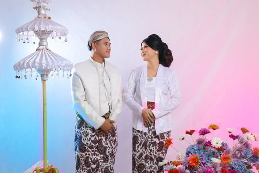 A pair of Asian boy and girl looking at each other cheerfully formally wearing modern Javanese traditional clothes, white velvet bridal kebaya, with a prewedding concept on a white studio background photo