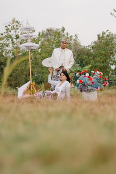 couple young indonesia male and female lovers smiling, women holding umbrellas sitting under modern Javanese traditional clothing, bridal white velvet kebaya in an outdoor barren garden photo