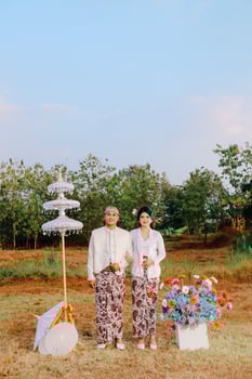 full length couple young indonesia men and women standing side by side in the middle of decorations wearing modern Javanese traditional clothes, white velvet for the bride in an outdoor barren garden photo